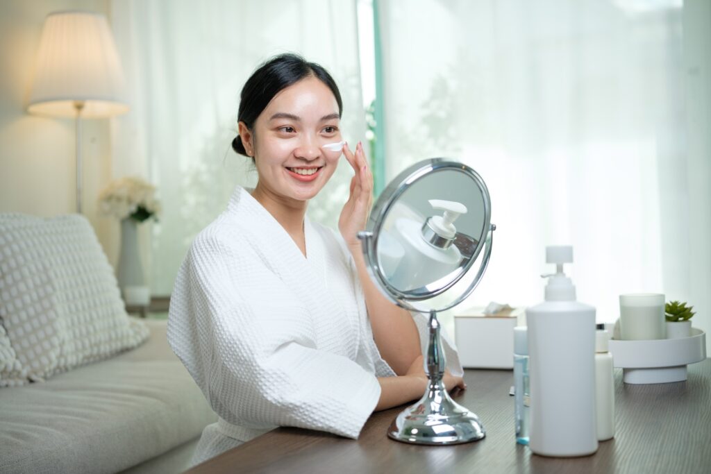 Woman applying moisturizer in her morning skincare routine under natural light, showcasing healthy glowing skin.