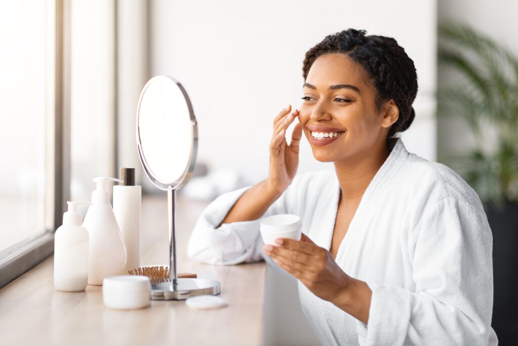 Woman applying a simple skincare routine at home with a few essential products on the counter.