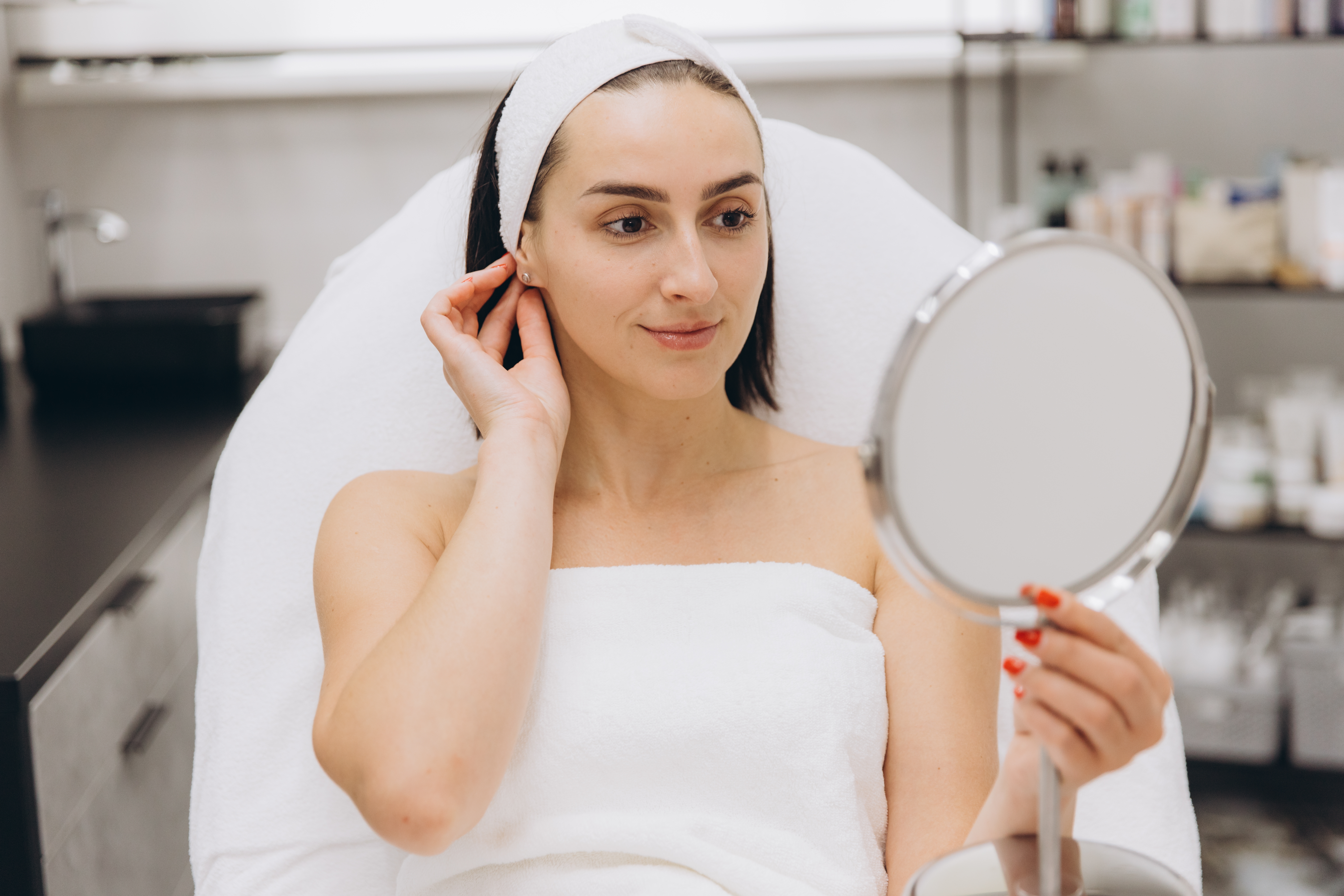 Woman looking in the mirror with glowing skin, showing the benefits of regular facials.