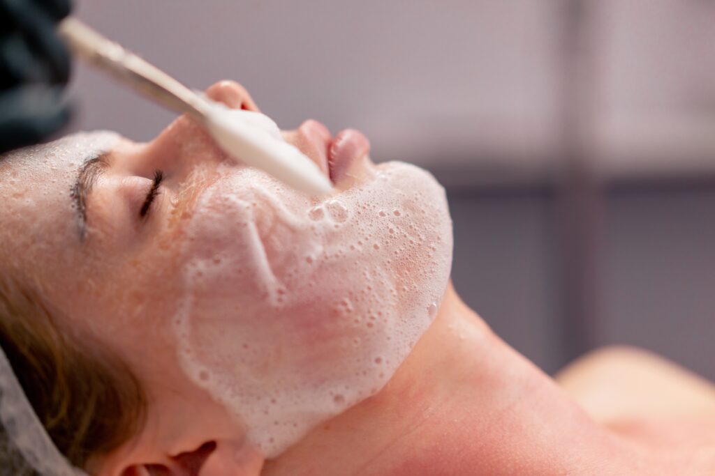 Client relaxing during a professional facial while an esthetician performs a cleansing and skincare treatment.
