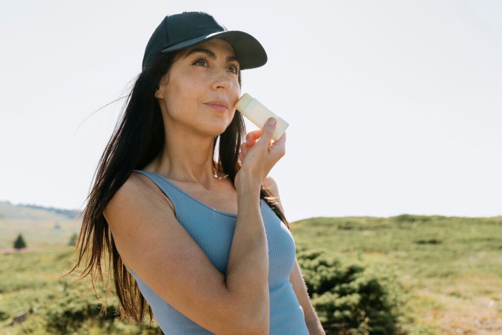 Woman applying lightweight sunscreen as part of an anti-aging skincare routine in bright natural sunlight.