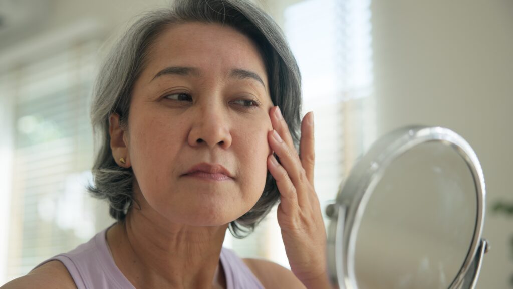 Woman looking at her  irritated skin in the mirror.