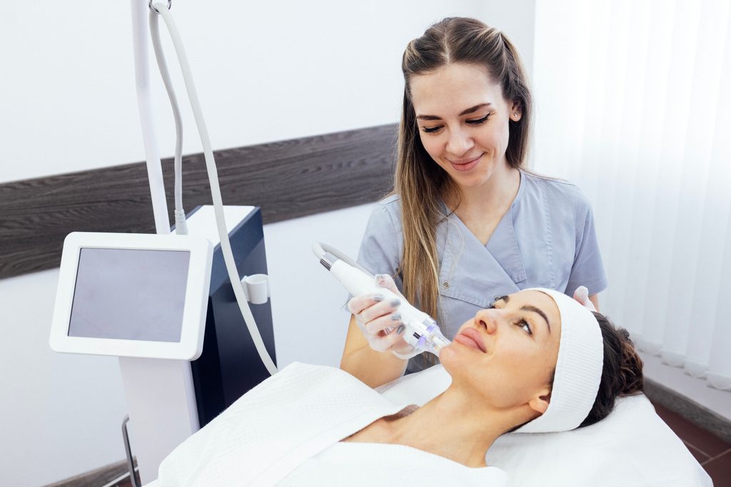 Esthetician performing a professional nano infusion facial while explaining the differences between nano infusion and micro-needling treatments.