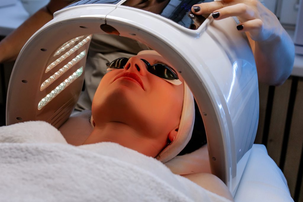 Client wearing protective goggles beneath an LED light panel during a facial treatment.