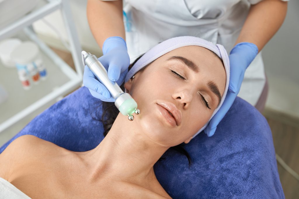Esthetician using a professional microcurrent facial device along a client’s jawline for gentle facial toning and sculpting.